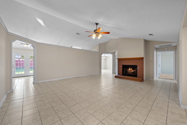 unfurnished living room featuring ceiling fan, light tile patterned floors, a textured ceiling, a brick fireplace, and vaulted ceiling