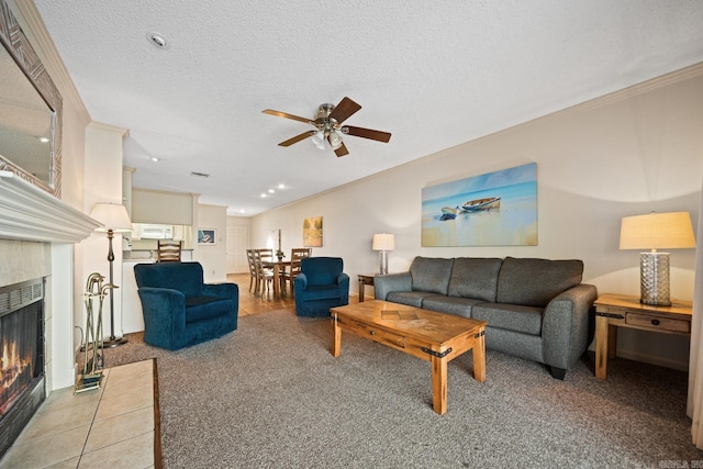 carpeted living room featuring ornamental molding, a textured ceiling, a tiled fireplace, and ceiling fan