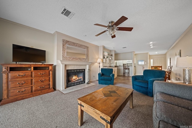 carpeted living room featuring crown molding, a textured ceiling, a tile fireplace, and ceiling fan