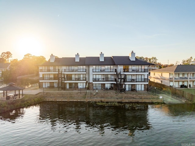 back house at dusk featuring a water view, a gazebo, and a balcony