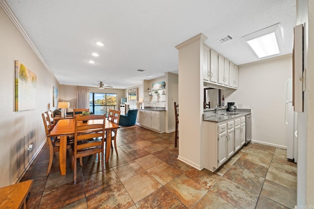 kitchen with white cabinets, ceiling fan, ornamental molding, a skylight, and sink