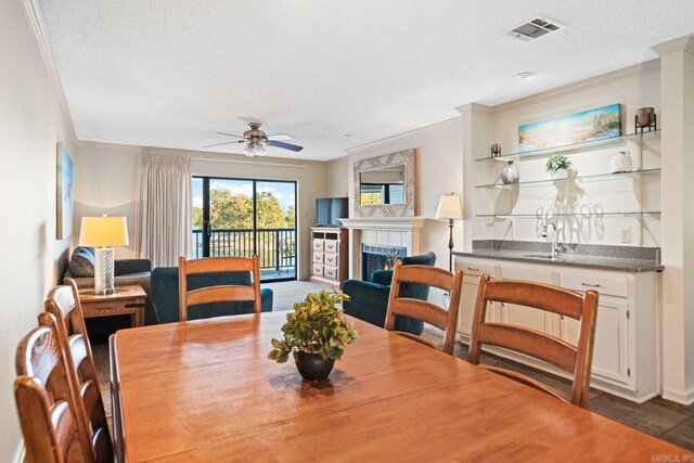 dining area featuring ceiling fan, a textured ceiling, ornamental molding, and a fireplace