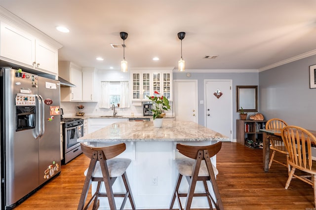 kitchen with a kitchen island, hanging light fixtures, white cabinets, light wood-type flooring, and appliances with stainless steel finishes