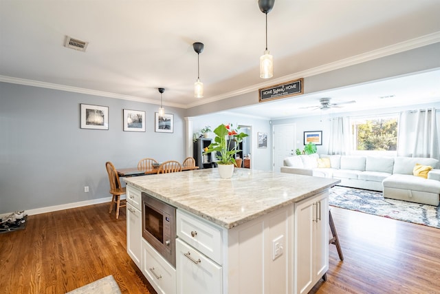 kitchen with a kitchen island, stainless steel microwave, a kitchen breakfast bar, hanging light fixtures, and white cabinetry