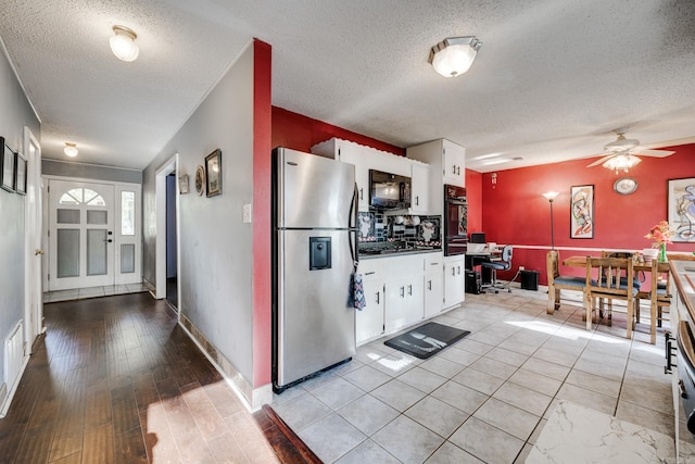 kitchen with light wood-type flooring, a textured ceiling, white cabinetry, black oven, and stainless steel refrigerator