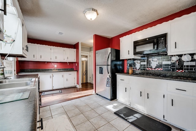 kitchen featuring tasteful backsplash, black appliances, light tile patterned flooring, a textured ceiling, and white cabinetry