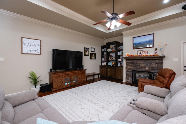 living room with ornamental molding, a stone fireplace, wood-type flooring, and ceiling fan