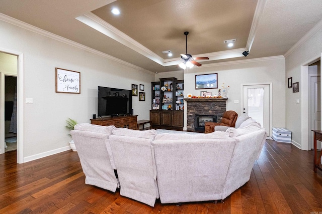 living room featuring a stone fireplace, ornamental molding, a raised ceiling, dark hardwood / wood-style flooring, and ceiling fan