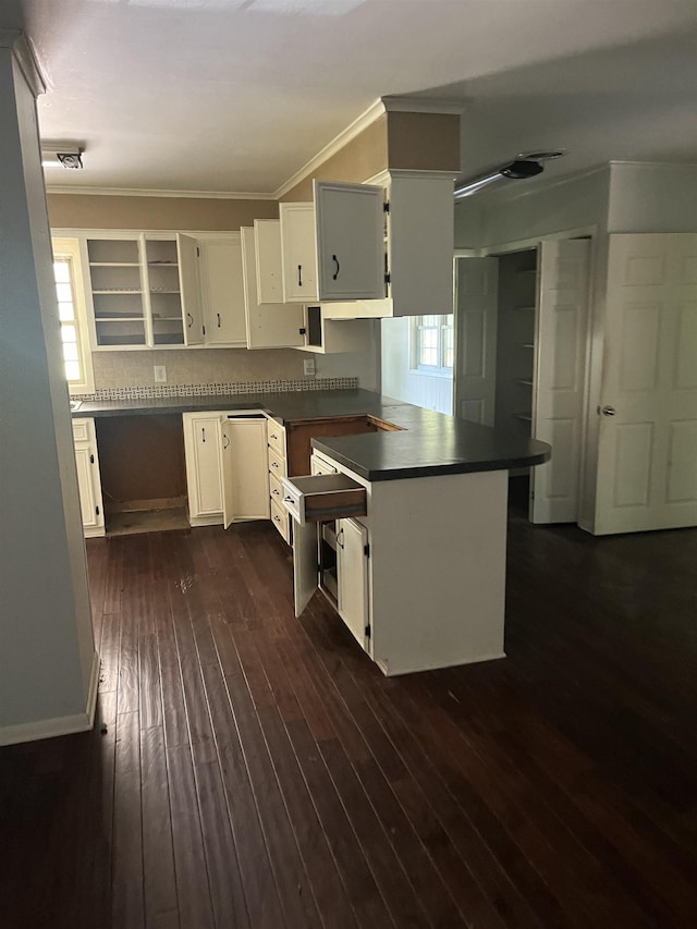 kitchen with dark wood-type flooring, crown molding, kitchen peninsula, and white cabinets