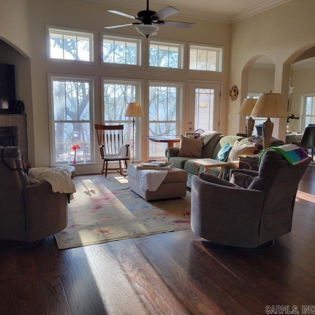 living room with a tiled fireplace, ceiling fan, wood-type flooring, a high ceiling, and crown molding