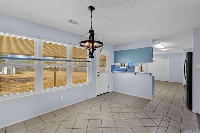 kitchen with kitchen peninsula, a textured ceiling, blue cabinetry, fridge, and light tile patterned flooring