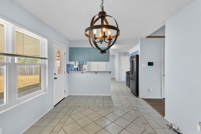 kitchen with a textured ceiling, kitchen peninsula, stainless steel fridge, light tile patterned floors, and a chandelier