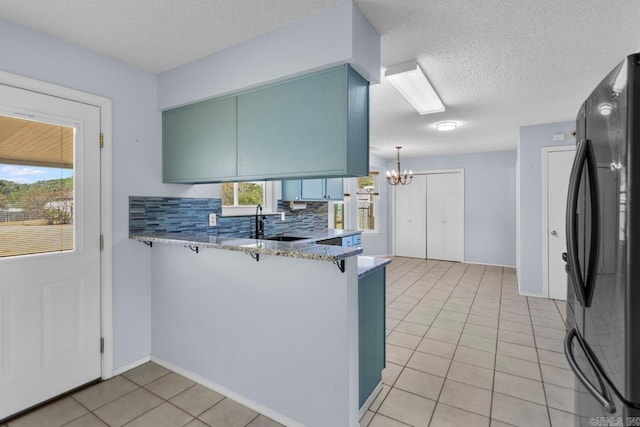 kitchen featuring plenty of natural light, light tile patterned floors, kitchen peninsula, and black fridge