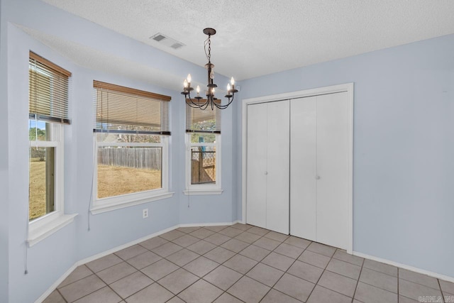 unfurnished dining area with a textured ceiling, a chandelier, and light tile patterned flooring