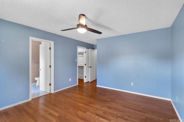 unfurnished bedroom with a spacious closet, connected bathroom, a closet, and wood-type flooring