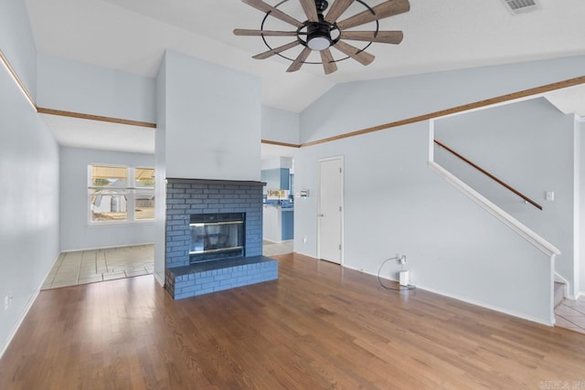 unfurnished living room with a brick fireplace, hardwood / wood-style flooring, ceiling fan, and vaulted ceiling