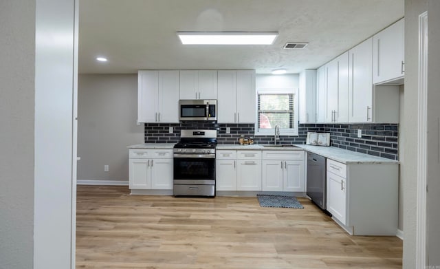 kitchen with appliances with stainless steel finishes, sink, light hardwood / wood-style floors, and white cabinets