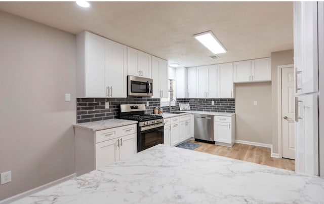 kitchen with stainless steel appliances, light hardwood / wood-style floors, white cabinetry, sink, and light stone counters