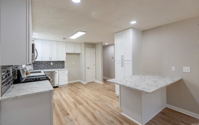 kitchen featuring light hardwood / wood-style floors, appliances with stainless steel finishes, light stone counters, backsplash, and white cabinets