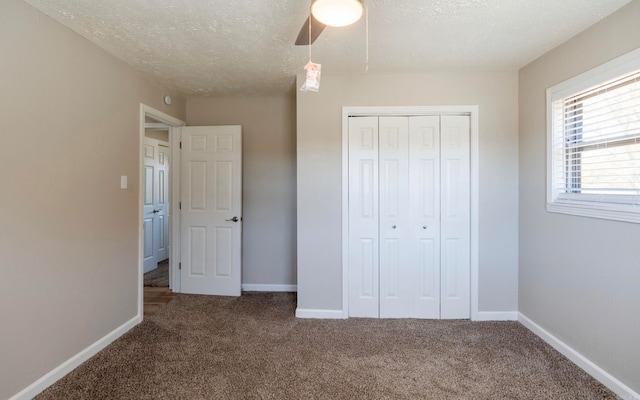 unfurnished bedroom with a closet, a textured ceiling, dark colored carpet, and ceiling fan