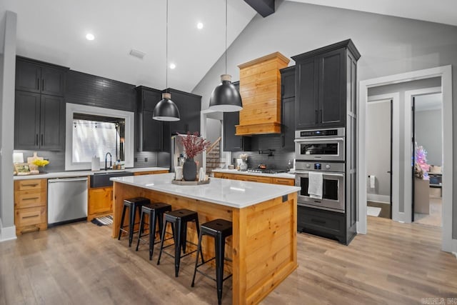 kitchen featuring decorative backsplash, vaulted ceiling with beams, light hardwood / wood-style flooring, stainless steel appliances, and a center island