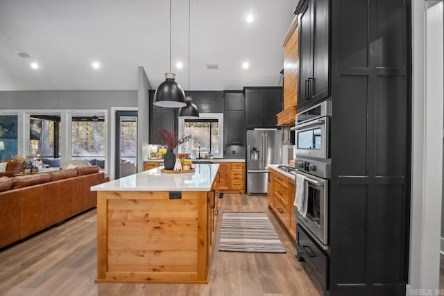 kitchen with hanging light fixtures, appliances with stainless steel finishes, light wood-type flooring, a center island, and sink