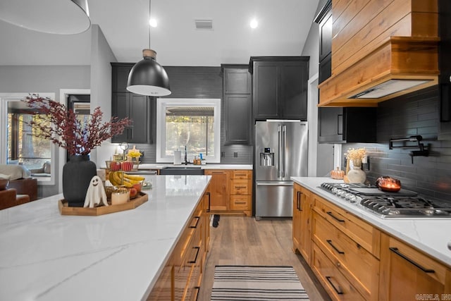 kitchen featuring light hardwood / wood-style floors, stainless steel appliances, decorative light fixtures, light stone counters, and decorative backsplash