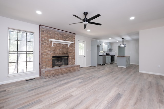 unfurnished living room featuring light hardwood / wood-style flooring, ceiling fan, a fireplace, and a wealth of natural light