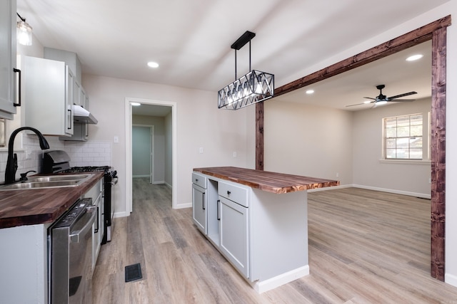 kitchen featuring tasteful backsplash, appliances with stainless steel finishes, hanging light fixtures, wooden counters, and light hardwood / wood-style flooring