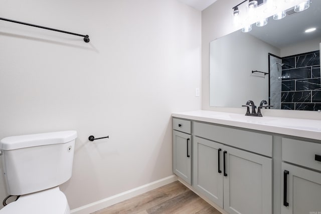 bathroom with vanity, toilet, hardwood / wood-style flooring, and tiled shower