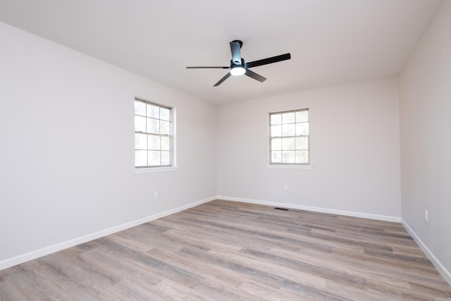 empty room featuring ceiling fan, a wealth of natural light, and light wood-type flooring