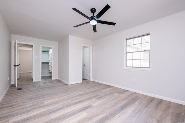 unfurnished bedroom featuring light hardwood / wood-style flooring, a walk in closet, a closet, and ceiling fan