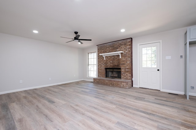 unfurnished living room featuring light hardwood / wood-style flooring, ceiling fan, plenty of natural light, and a brick fireplace