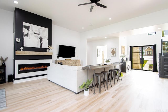 living room featuring light hardwood / wood-style flooring, a large fireplace, and ceiling fan