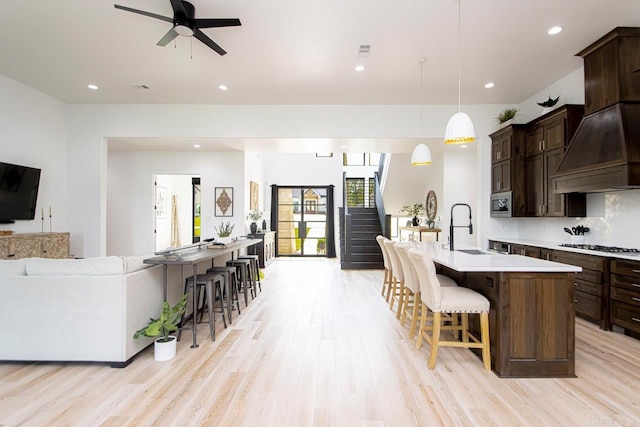 kitchen featuring a kitchen bar, light wood-type flooring, hanging light fixtures, custom range hood, and a center island with sink