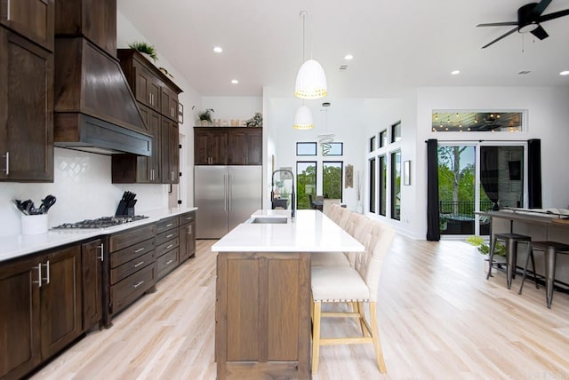 kitchen featuring sink, an island with sink, hanging light fixtures, stainless steel appliances, and custom range hood