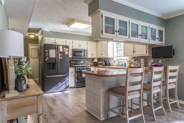 kitchen with kitchen peninsula, white cabinets, backsplash, light wood-type flooring, and stainless steel appliances