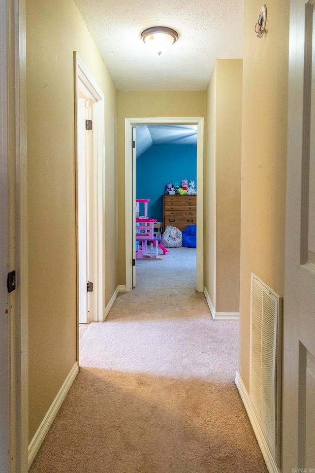 hallway with lofted ceiling, a textured ceiling, and light colored carpet