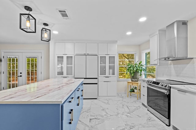 kitchen featuring wall chimney range hood, stainless steel electric range, hanging light fixtures, a kitchen island, and white cabinetry