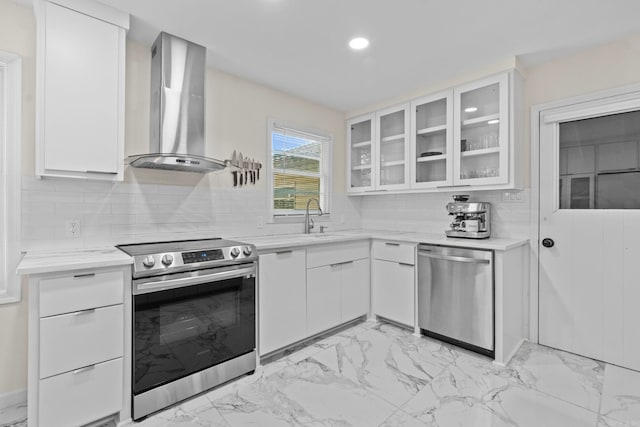 kitchen featuring tasteful backsplash, wall chimney range hood, sink, white cabinetry, and stainless steel appliances