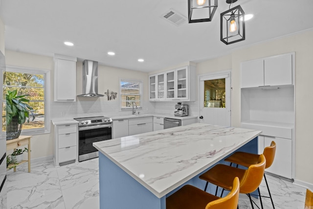 kitchen featuring stainless steel appliances, wall chimney range hood, a kitchen island, and white cabinets