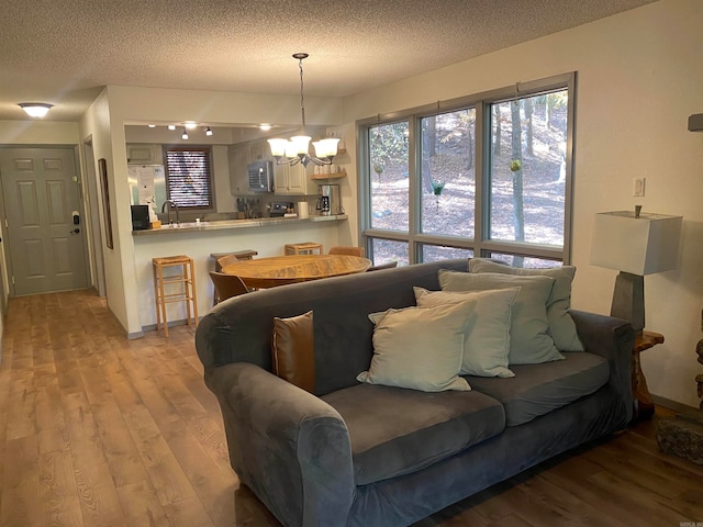 living room with sink, a textured ceiling, light hardwood / wood-style flooring, and a chandelier