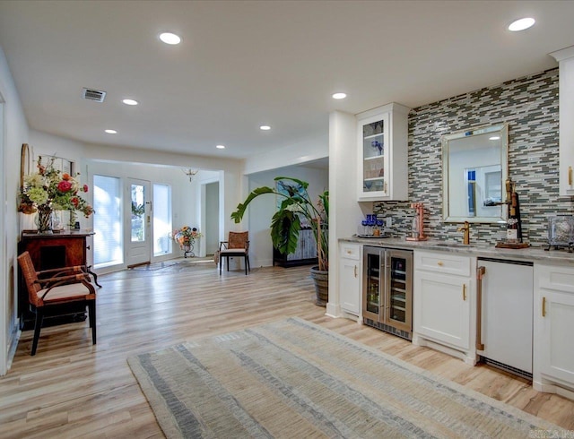 bar with backsplash, white cabinets, light wood-type flooring, and beverage cooler