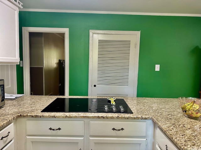 kitchen with black electric stovetop, white cabinets, light stone countertops, and crown molding