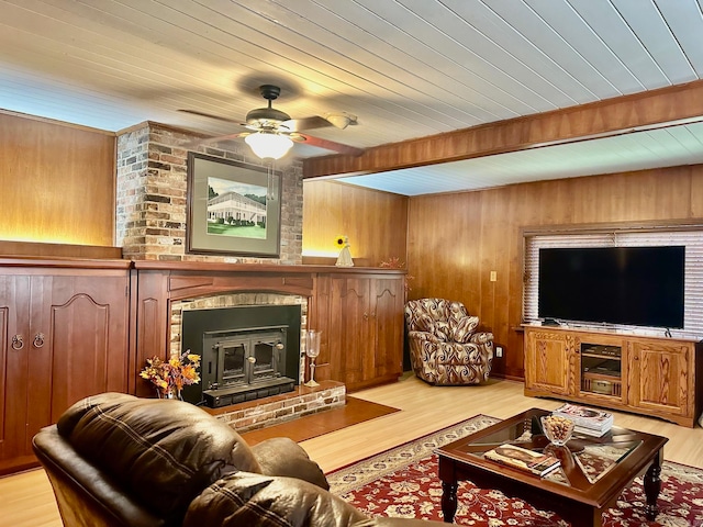 living room with a fireplace, wooden walls, light wood-type flooring, and ceiling fan