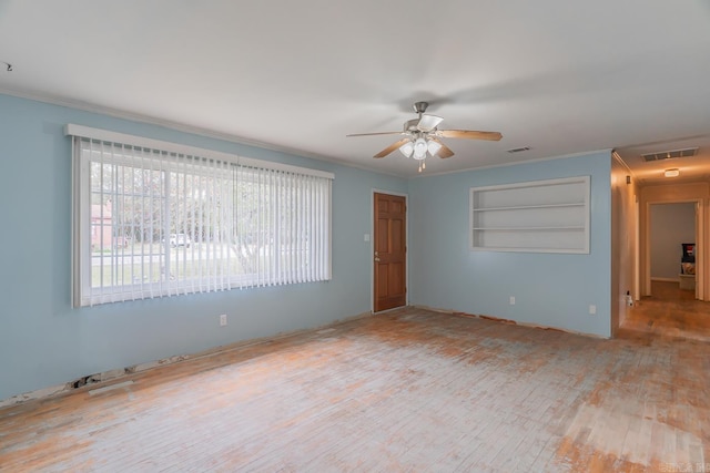 empty room with built in features, visible vents, a ceiling fan, ornamental molding, and wood finished floors