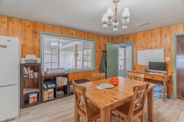 dining space featuring wood walls, light wood-type flooring, visible vents, and an inviting chandelier