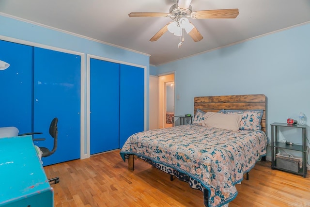 bedroom with ceiling fan, wood finished floors, two closets, and crown molding