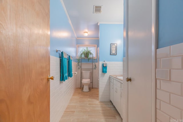 bathroom with crown molding, tile walls, visible vents, toilet, and wainscoting