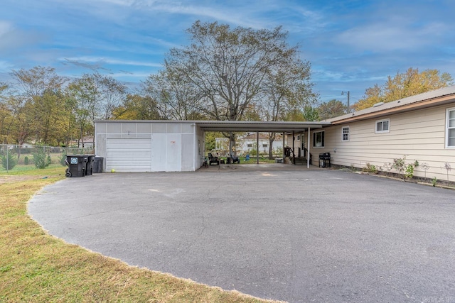 exterior space featuring a carport, fence, driveway, and an outdoor structure